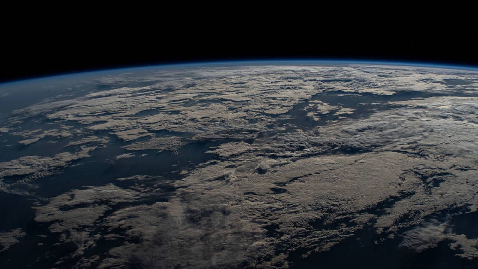 Earth’s curved blue atmosphere and cloud cover, photographed from the International Space Station.